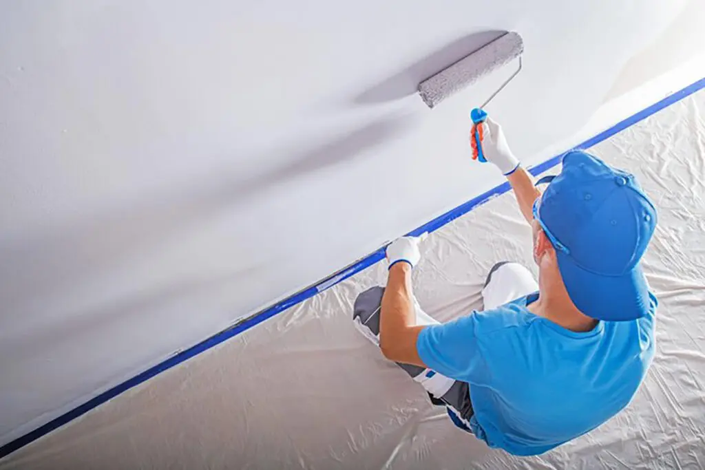 Interior painter rolling fresh white paint on a ceiling, illustrating how long does paint take to cure after interior painting
