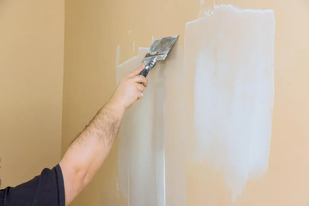 A professional applying skim coat compound to an interior wall during surface preparation after wallpaper removal.