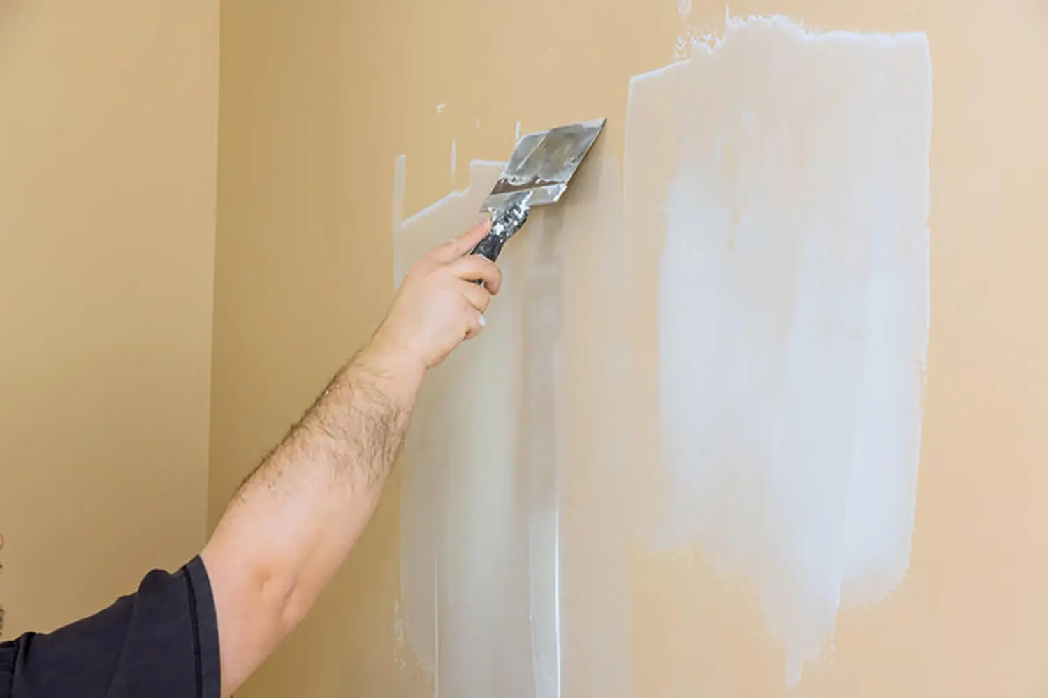 A professional applying skim coat compound to an interior wall during surface preparation after wallpaper removal.