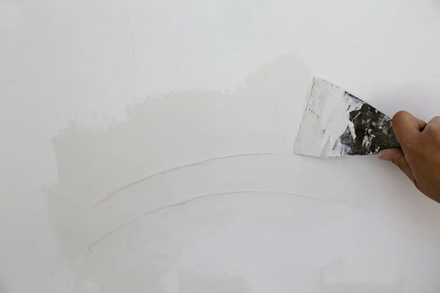 A hand applying joint compound to an interior wall during professional drywall repair before painting.